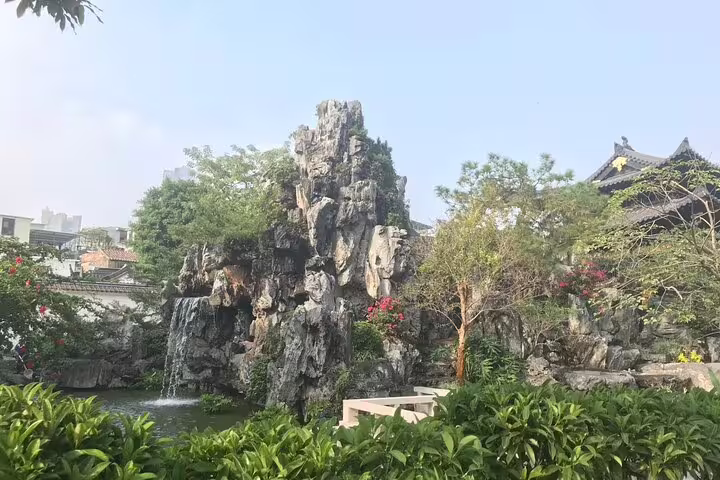 Tranquil garden scene in Guangzhou featuring lush greenery, a rock waterfall, and traditional architecture on a day tour.