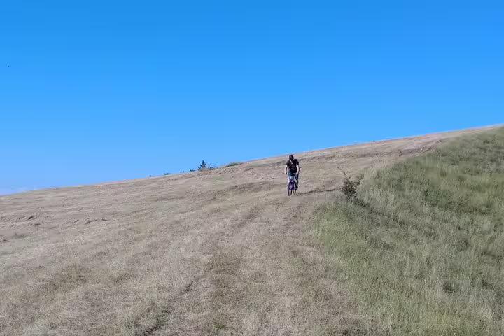 Cyclist riding uphill on a grassy trail in Transylvania countryside under clear blue sky