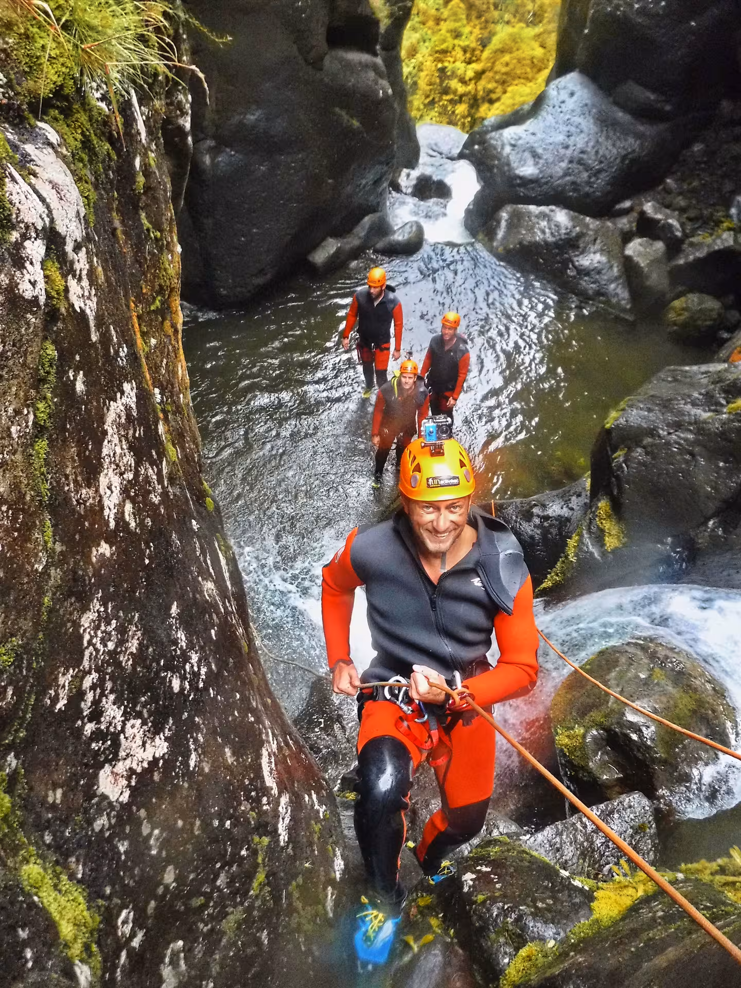 Guided canyoning in Lombadas Praia gorge, group in wetsuits and helmets climbing beside river and rocks
