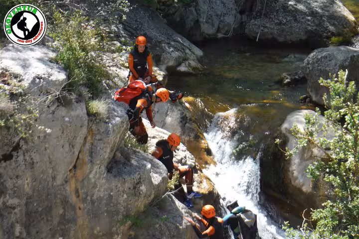 Guided canyoning in Teruel with helmets and wetsuits descending rocks beside a clear canyon waterfall