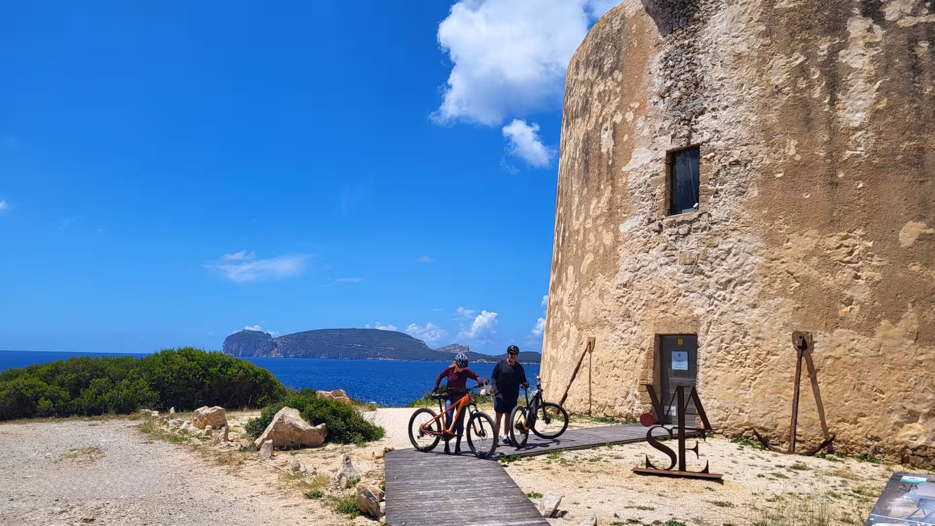 Cyclists enjoy a guided ebike tour near Capo Caccia, Alghero, showcasing scenic coastal views and historic architecture.