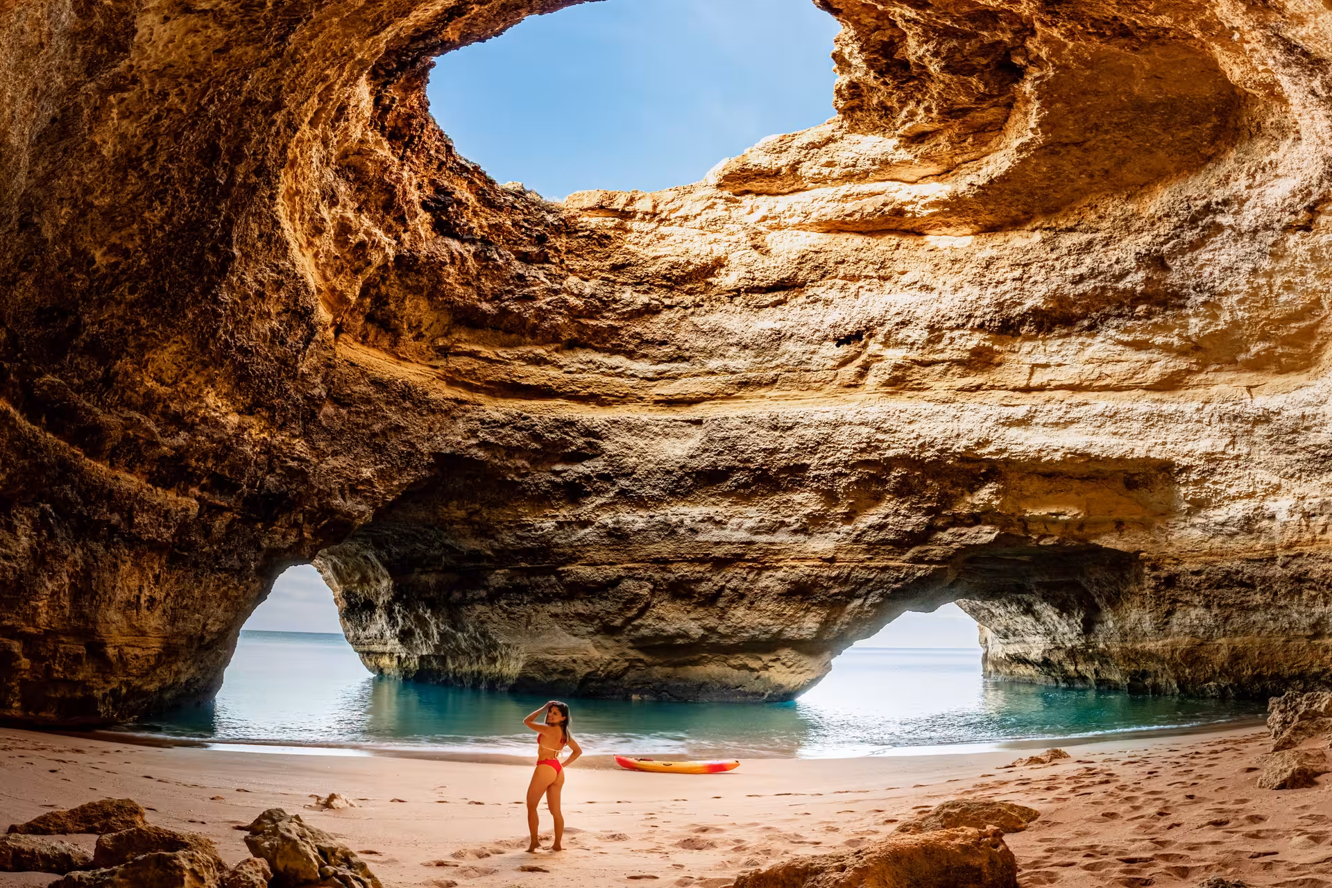 Person standing in a majestic sea cave with a kayak on the sand, ideal for guided tours.