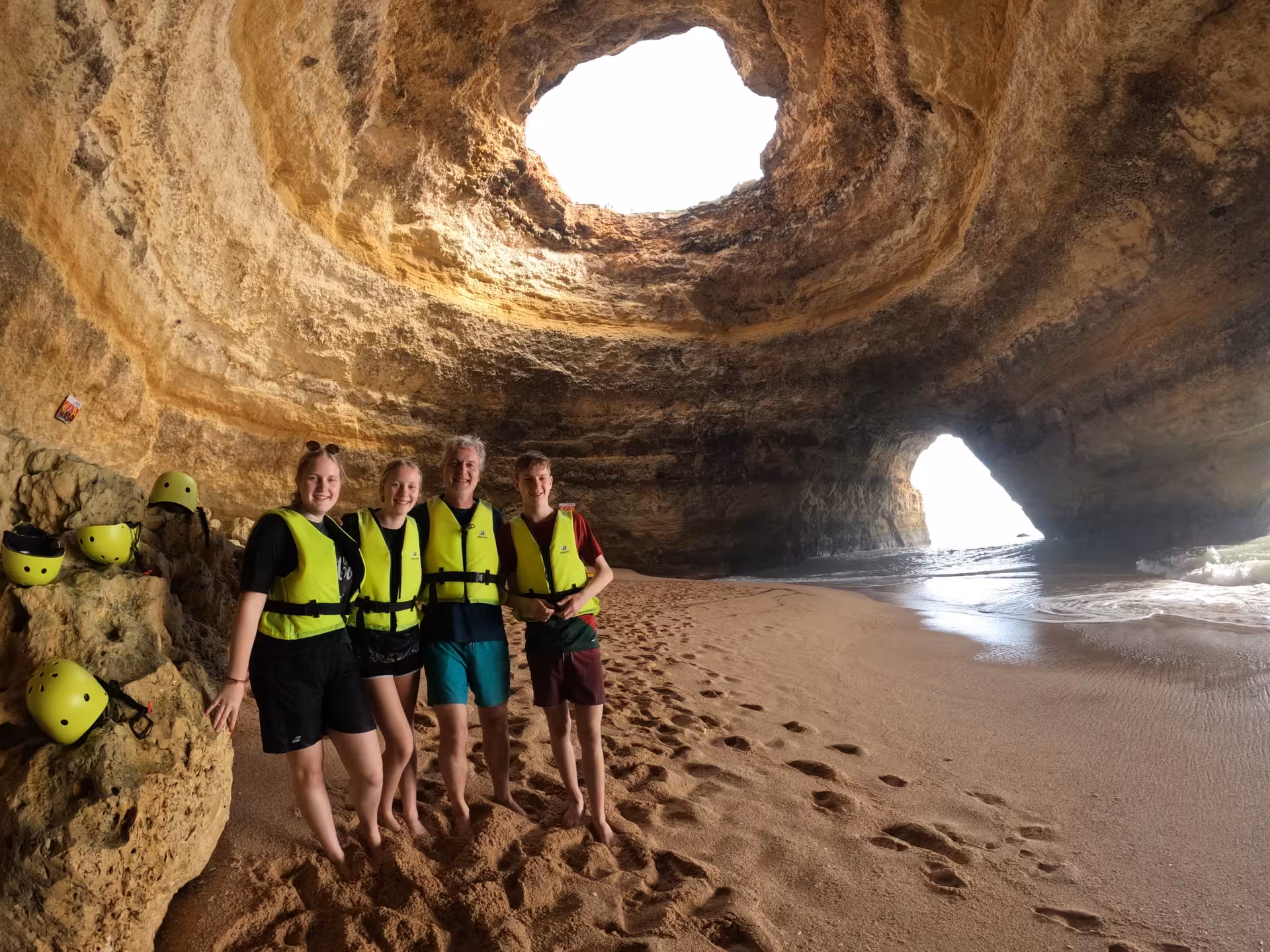 Group enjoying guided kayak tour inside stunning coastal cave with sandy beach and helmets.