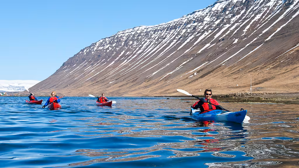 Guided sea kayaking in a fjord beneath snow-streaked mountains, ideal add-on to a bike and kayak combo.