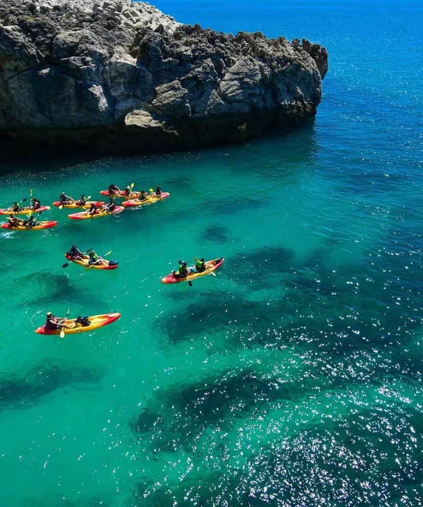 Guided sea kayaking in Sesimbra, Portugal, paddling turquoise waters by rocky cliffs on an Arrábida coast tour