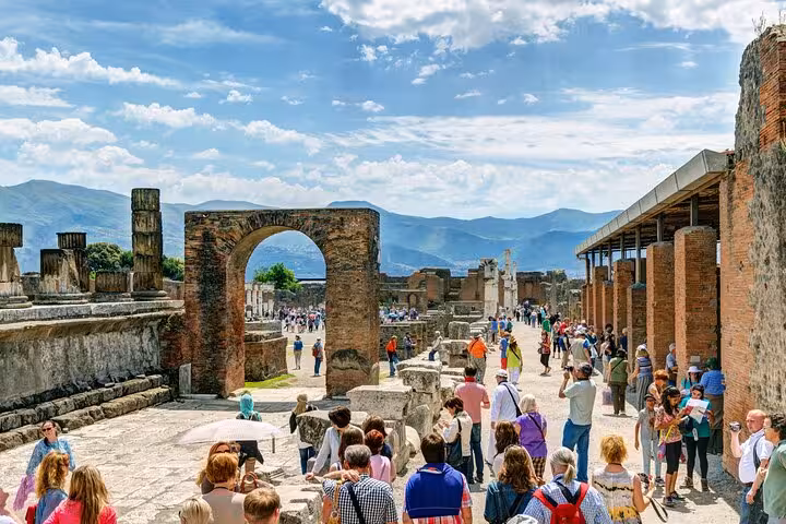 Tourists explore the bustling streets of ancient Pompeii under a bright blue sky on a guided tour with lunch.