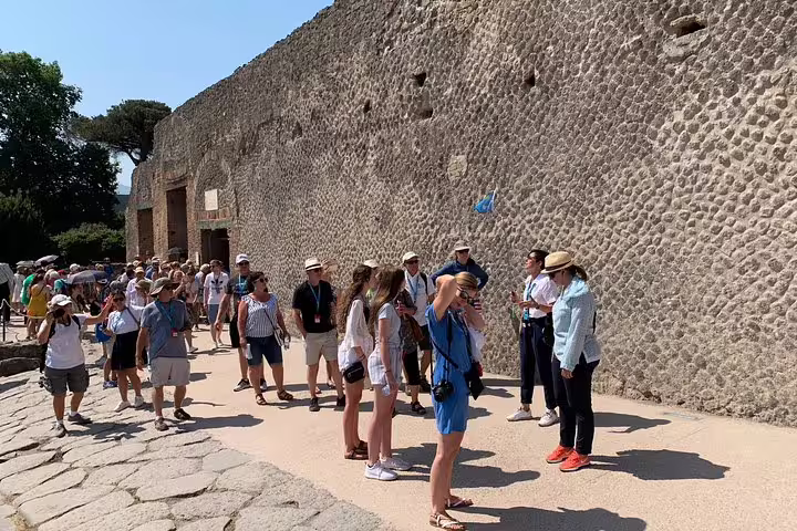 A group of tourists on a guided tour from Sorrento walk along ancient walls in Pompeii, exploring Roman history and culture.