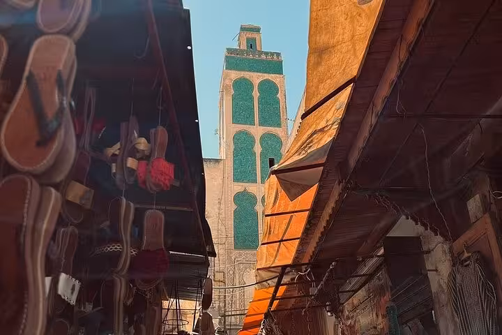 Bustling market street with a view of a historic mosque tower in the Old Medina of Fez.