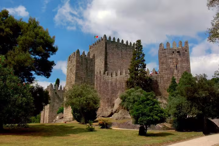 Majestic Guimarães Castle in Portugal with its medieval stone walls and lush surrounding greenery under a blue sky.