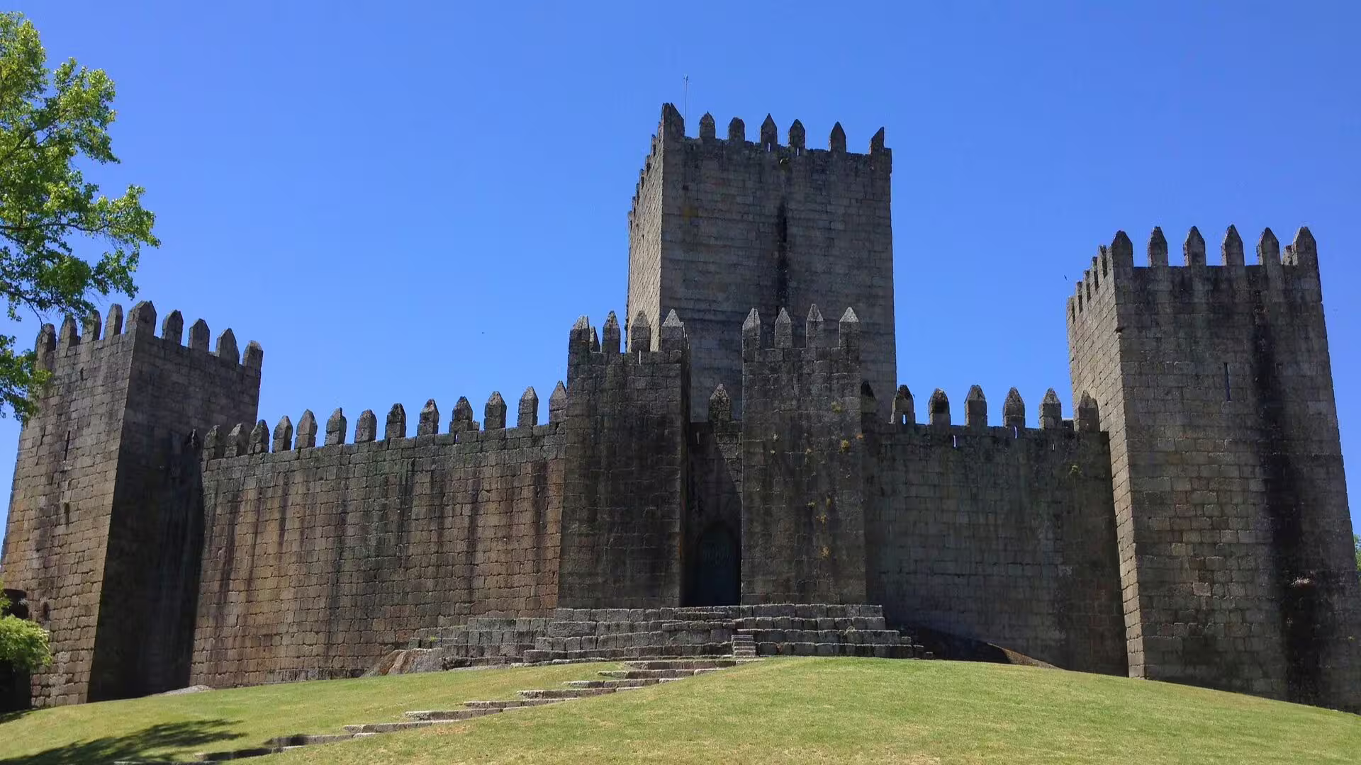 Guimarães Castle's imposing stone walls and towers under a bright blue sky, symbolizing Portugal's medieval heritage.