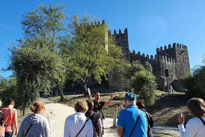 Visitors explore the historic Guimarães Castle, guided through lush surroundings and ancient stone walls.