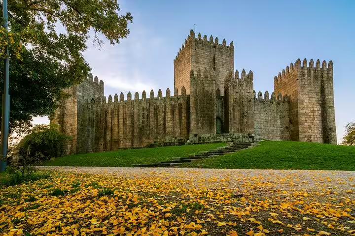 Explore the medieval charm of Guimarães Castle on a private half-day tour from Porto, surrounded by autumn foliage.