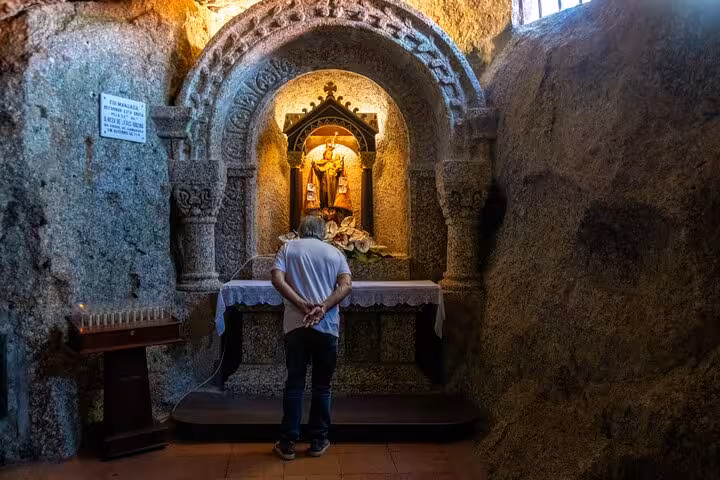 Visitor admiring a religious shrine inside a stone alcove, highlighting spiritual heritage in Guimarães, Portugal on a full-day tour.