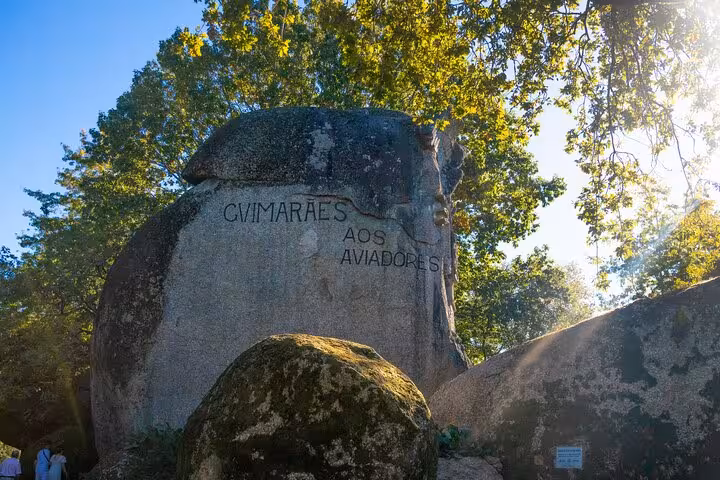 Engraved stone monument in Guimarães dedicated to aviators, surrounded by lush trees on a Portugal cultural tour.