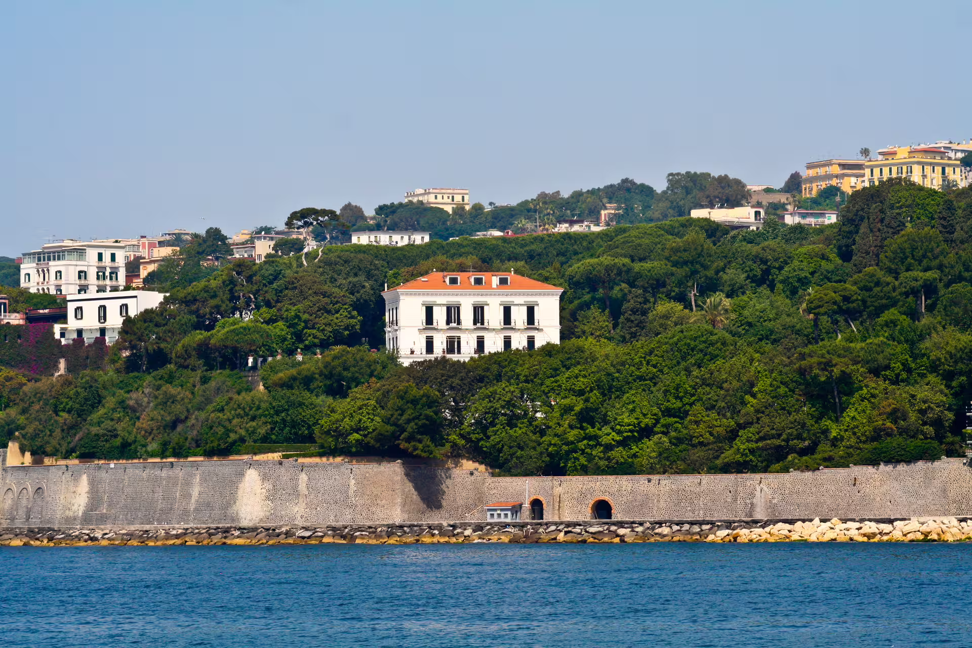 Elegant seaside villas and lush green hills above the Gulf of Naples, seen from a catamaran on a full-day coastal cruise