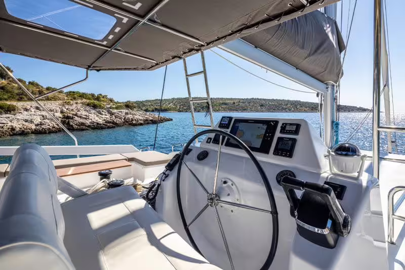 Modern catamaran helm with shaded cockpit overlooking turquoise waters and rocky coastline in the Gulf of Naples