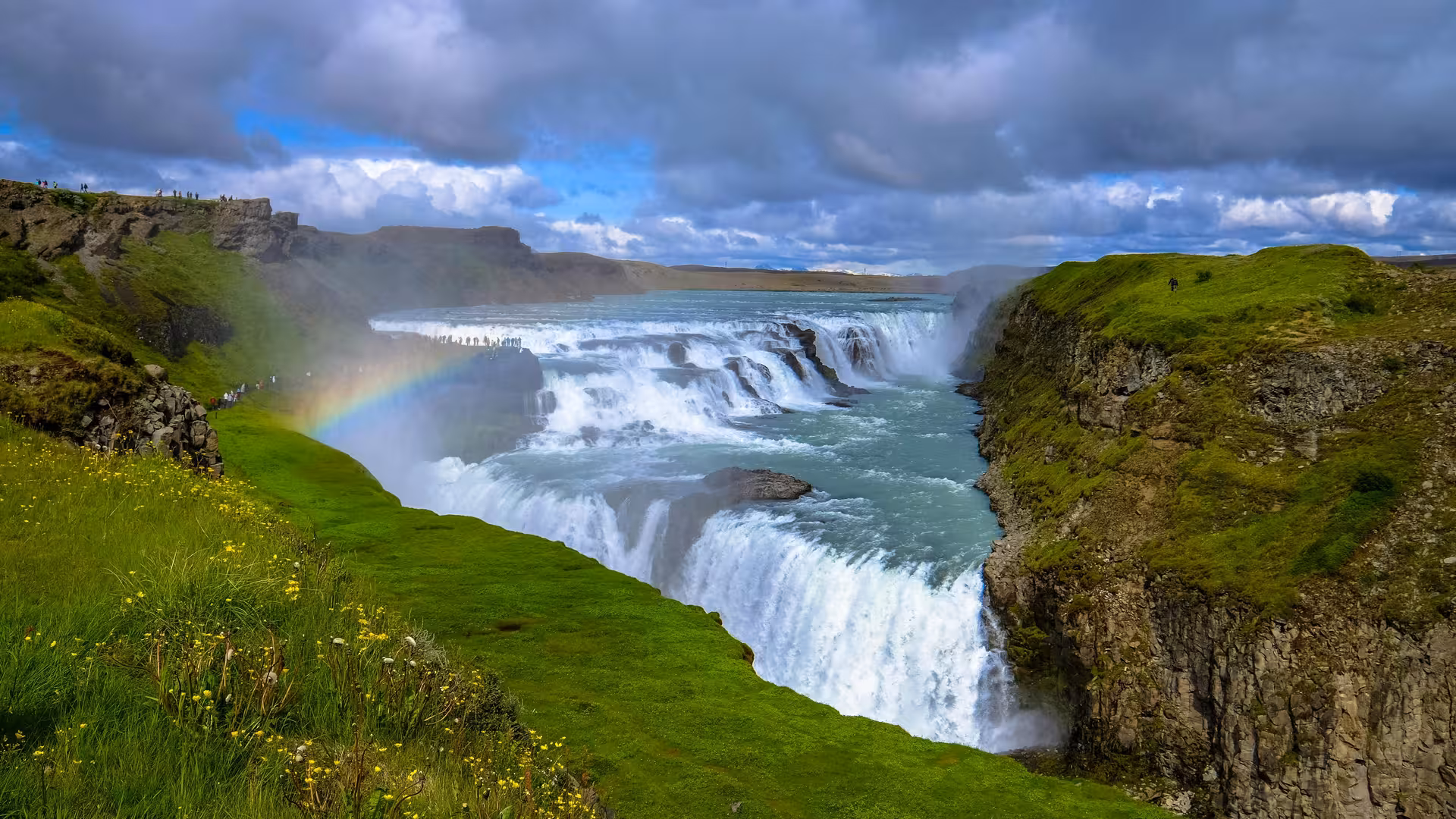 Breathtaking view of Gullfoss waterfall with a rainbow over lush green cliffs, a must-see on the Golden Circle Private Tour.