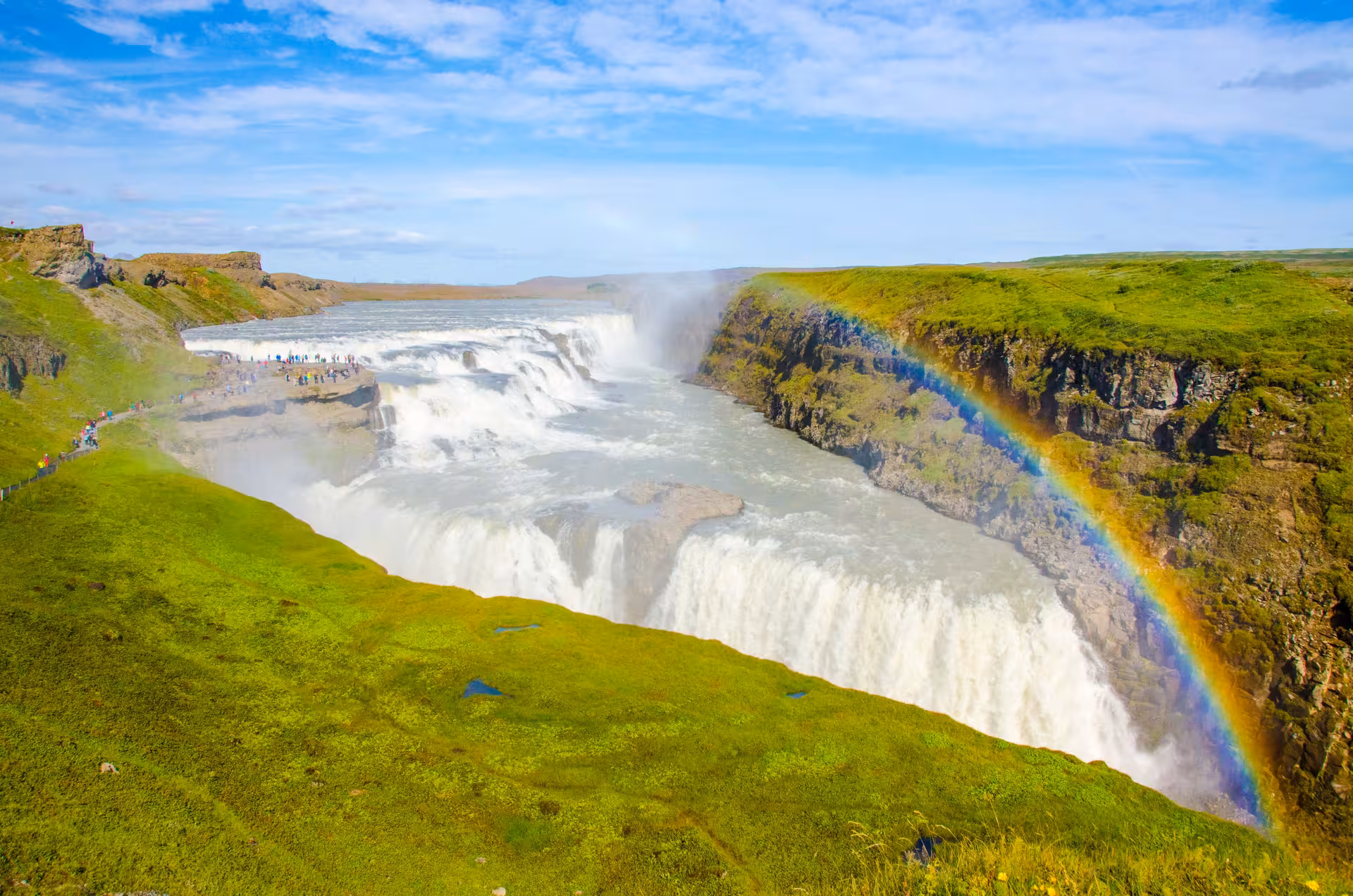 Stunning view of Gullfoss waterfall with vibrant rainbow under clear blue skies in Iceland's Golden Circle.