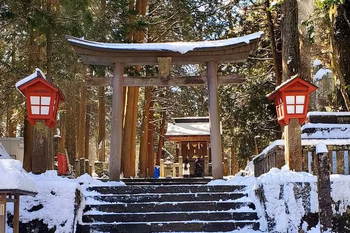 Snow-covered Torii gate and red lanterns at a serene shrine in Hakone forest, perfect for a Tokyo private tour.
