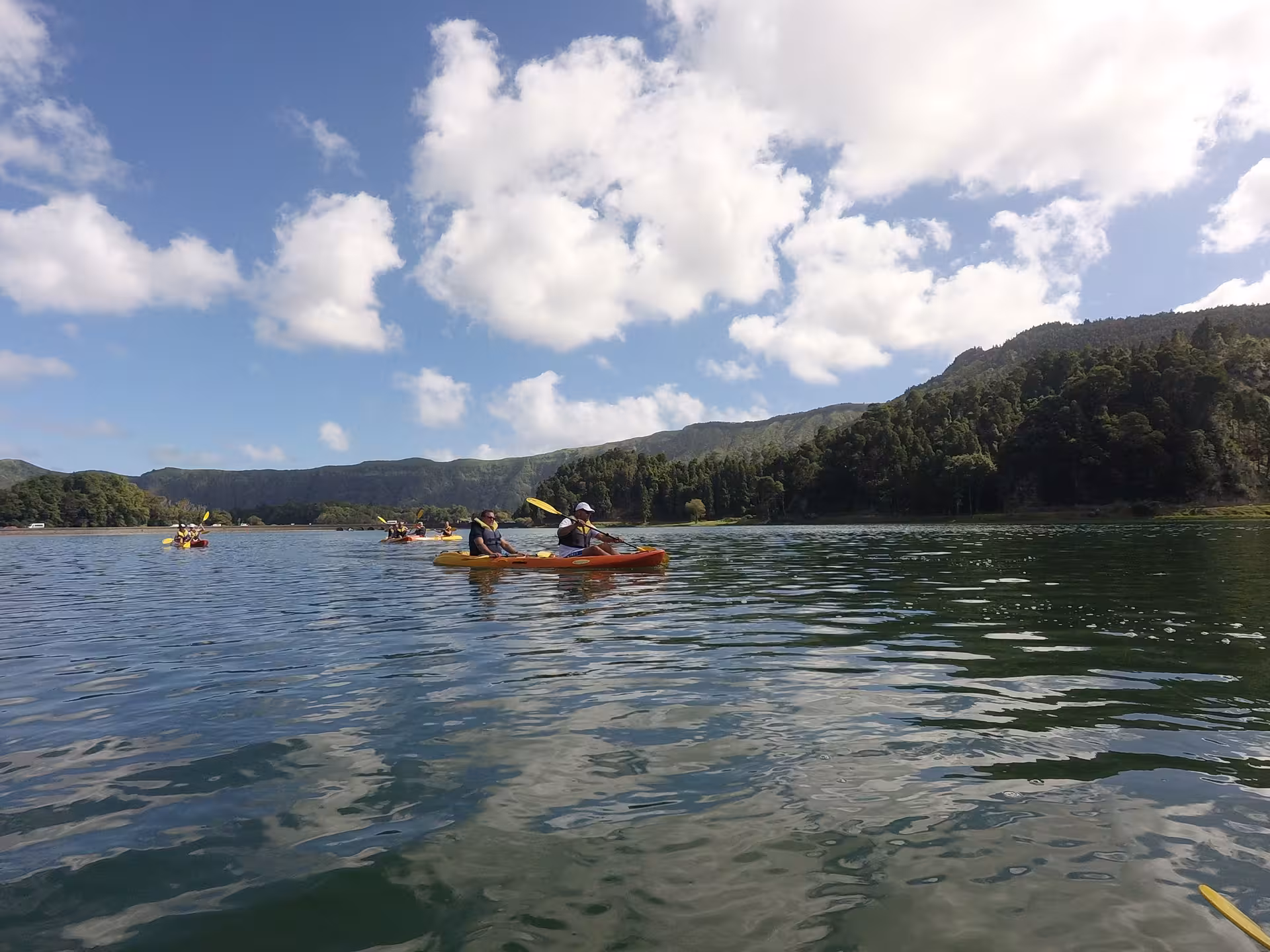 Half-day canoeing experience on a scenic mountain lake, group paddling on calm water under blue sky and clouds