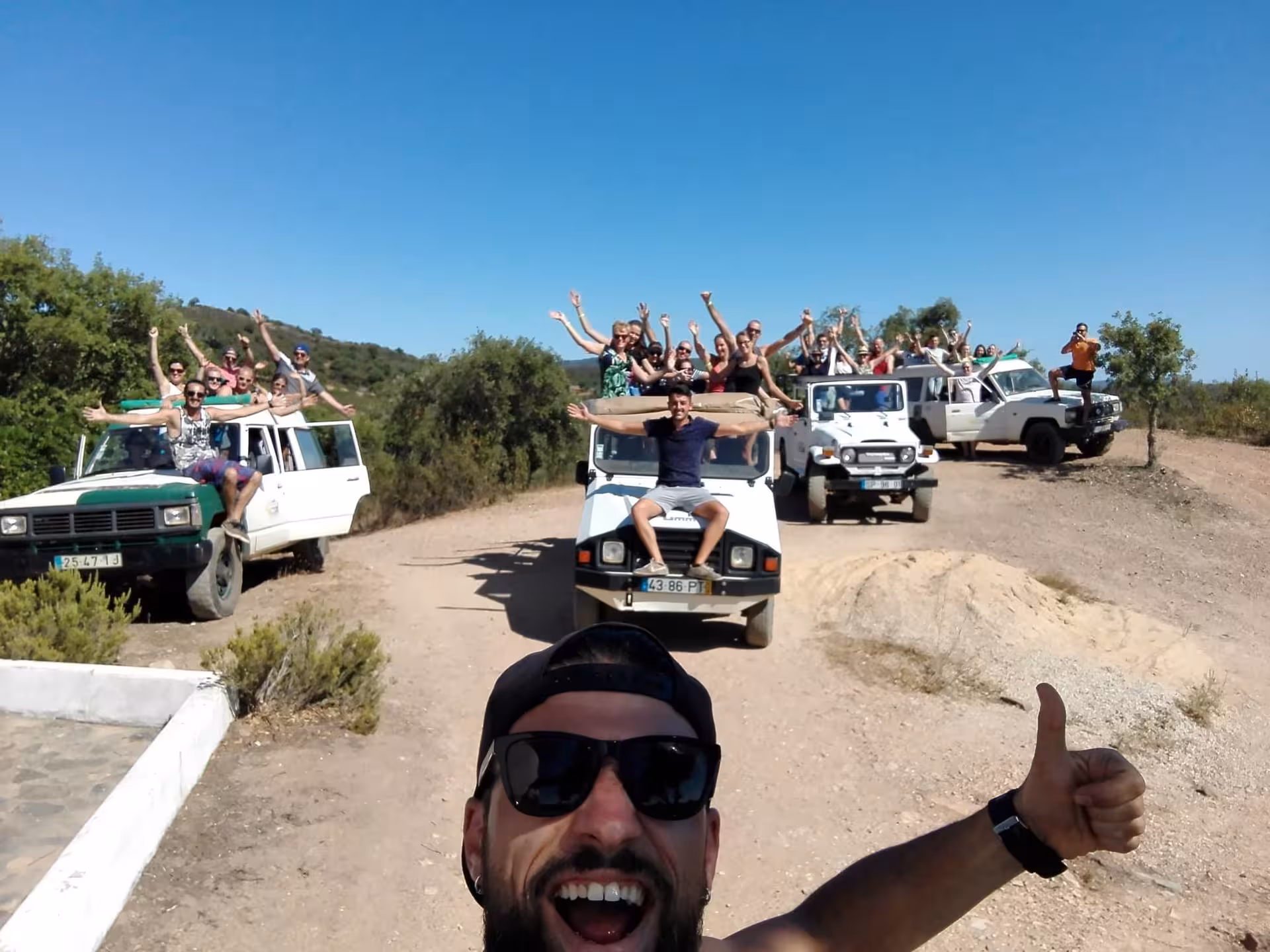 Friends on multiple jeeps celebrating during Half Day Jeep Safari in Algarve, off-road adventure under clear blue skies