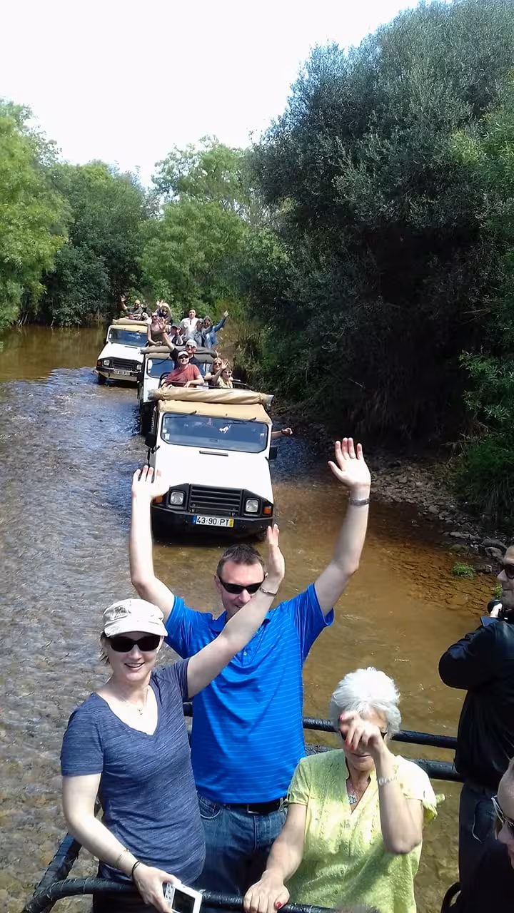 Group on Half Day Jeep Safari in Algarve driving jeeps through shallow river, waving and enjoying lush countryside scenery