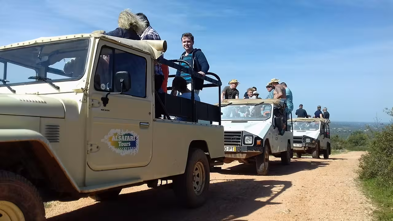 Open-top jeeps full of smiling tourists drive along a dusty Algarve track on a guided half day off-road safari tour
