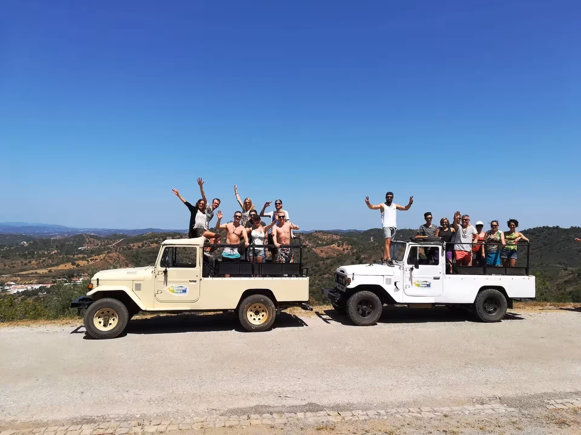 Two safari jeeps with excited travelers pose on a hilltop, enjoying panoramic Algarve countryside views on a jeep tour