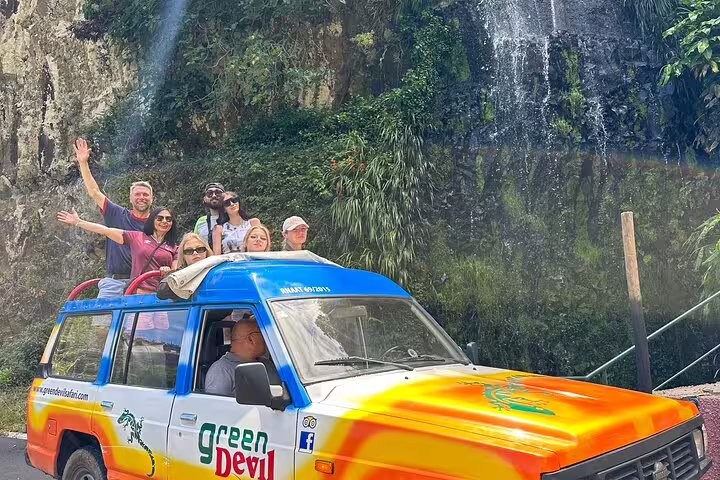 Group enjoying a scenic half-day jeep wine tour and sea cliff adventure next to a waterfall in a vibrant off-road vehicle.