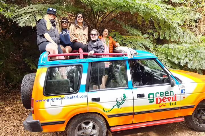 Group of tourists enjoying a scenic jeep tour through lush greenery on a half-day wine tasting and sea cliff adventure.