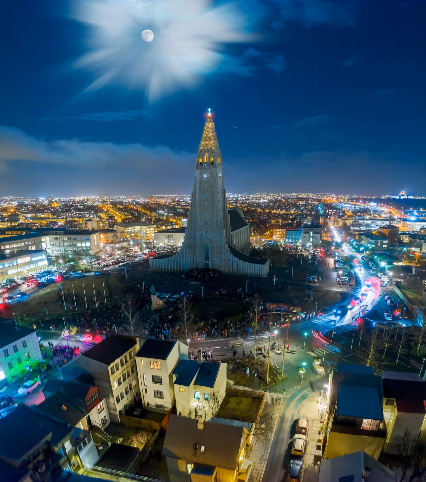 Night view of Hallgrimskirkja in Reykjavik illuminated under a full moon, showcasing Iceland's vibrant cityscape.