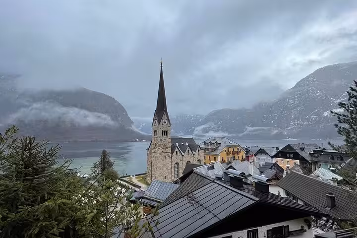 View of Hallstatt church spire and lakeside rooftops with misty Alps, highlight of Vienna to Hallstatt day tour