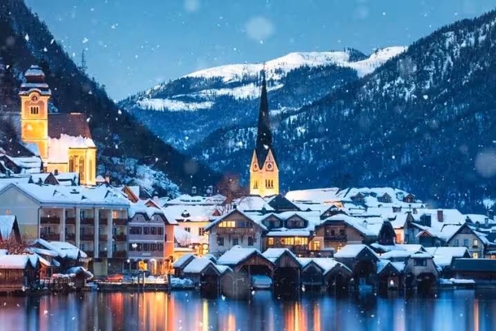 Hallstatt at dusk with lit church spire, snowy lakeside houses and reflections, Vienna private day tour