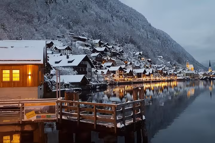 Snowy Hallstatt waterfront at dusk with glowing lights and reflections, highlight of Vienna to Hallstatt tour