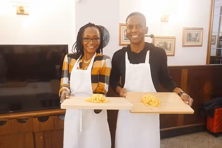 Two participants proudly display their handmade pasta at a cooking class in Rome, wearing aprons and smiling.