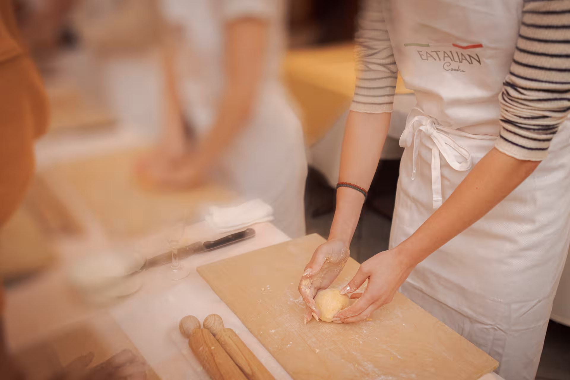 Close-up of hands kneading pasta dough on a wooden board in a fettuccine cooking class in Rome city center.
