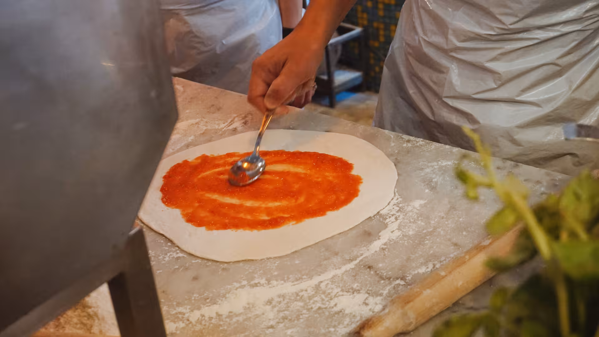 Hands spreading tomato sauce on pizza dough at Jazz Cafe's cooking class in Rome, Italy.