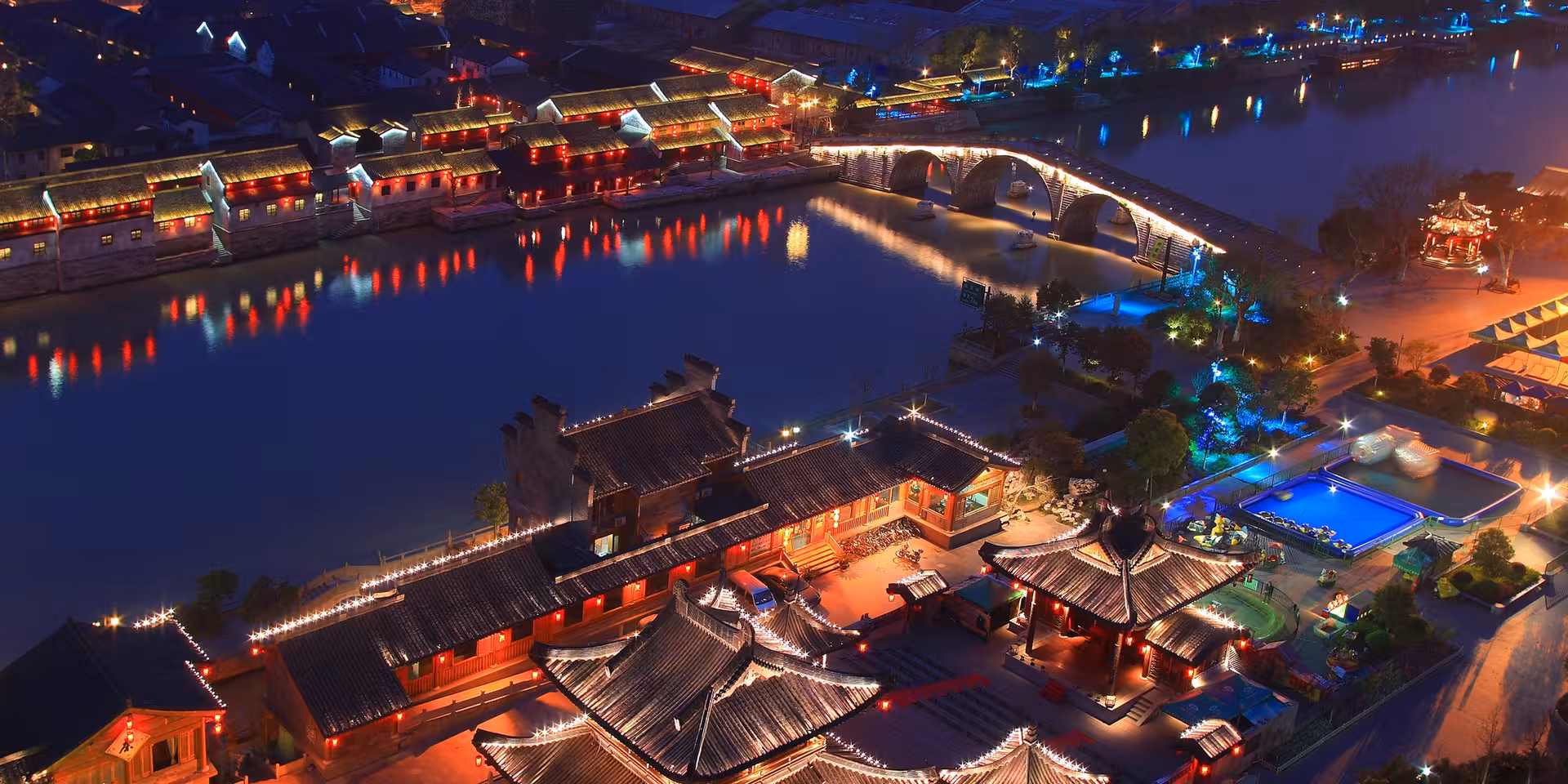 Vibrant night view of Hangzhou's ancient water town with illuminated traditional architecture and bridge.