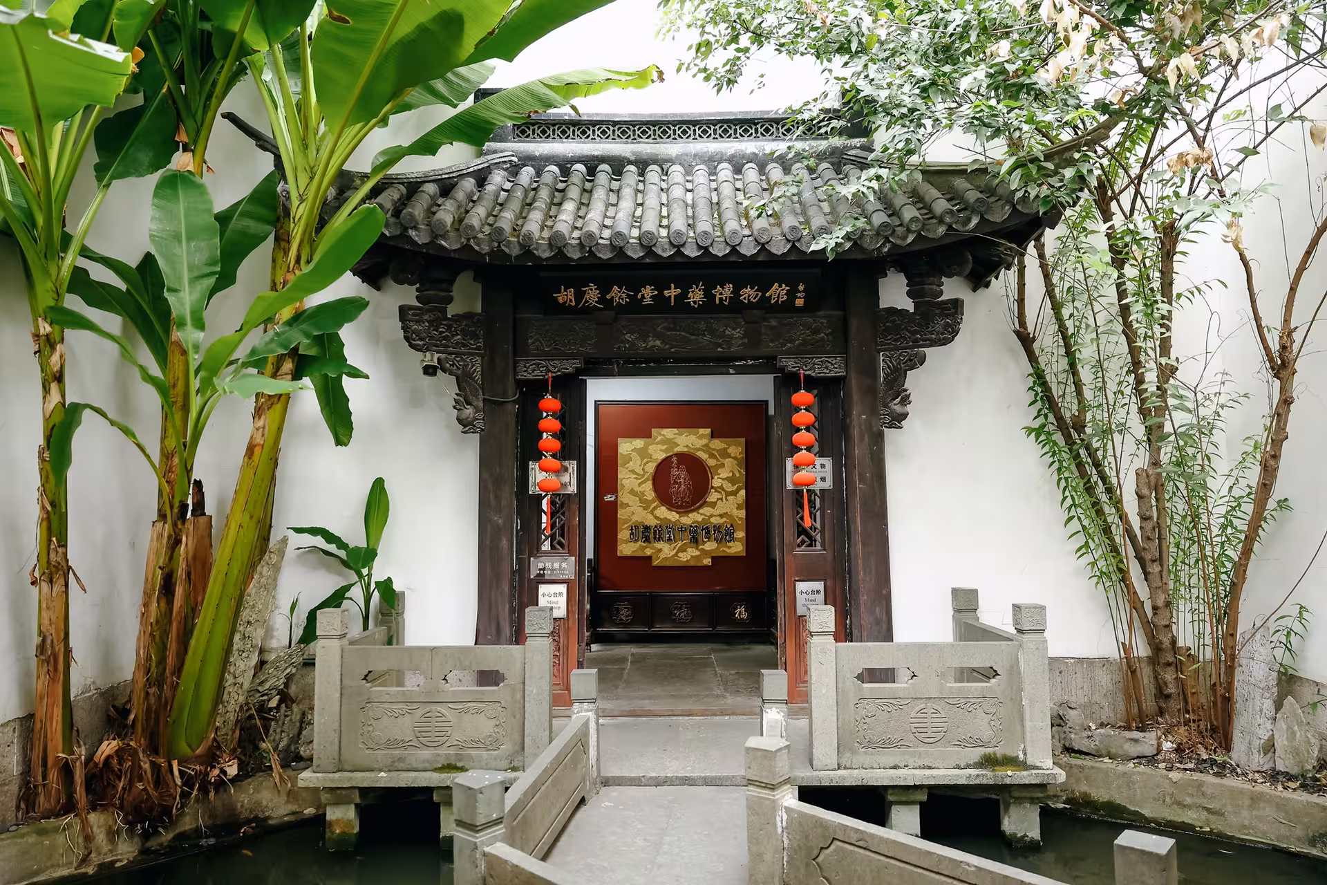 Entrance to a traditional Chinese herbal medicine museum in Hangzhou, surrounded by lush tropical plants and ornate carvings.