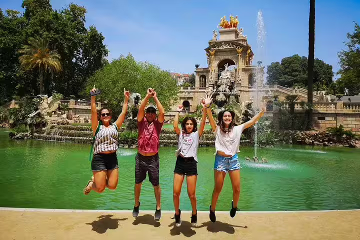 Group of happy tourists jumping in front of the iconic Cascada Monumental fountain in Barcelona's Ciutadella Park on a sunny day.