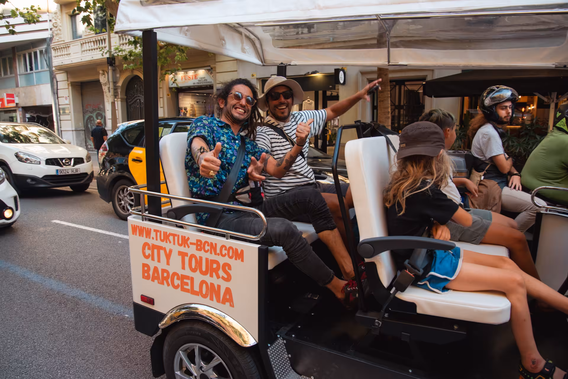 Happy travelers in an open-air tuk tuk on a Barcelona city street, enjoying the Welcome Tour Barcelona sightseeing