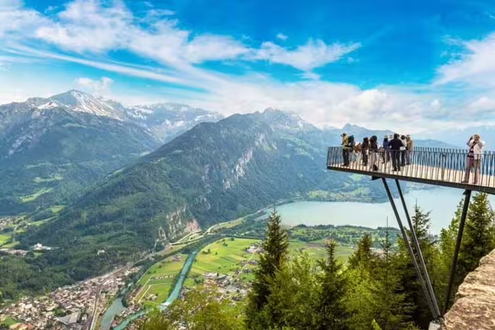 Tourists enjoy panoramic views from Harder Kulm's scenic platform overlooking Interlaken and the Swiss Alps.