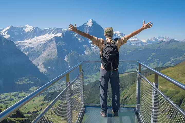 Traveler on Harder Kulm viewing platform with arms outstretched, admiring stunning Swiss Alps on Grindelwald day trip.