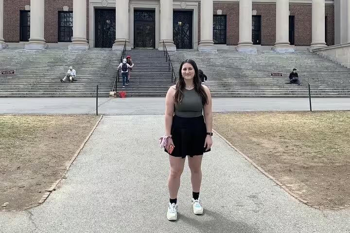 Young woman smiling in front of Harvard University's Widener Library steps on a sunny day