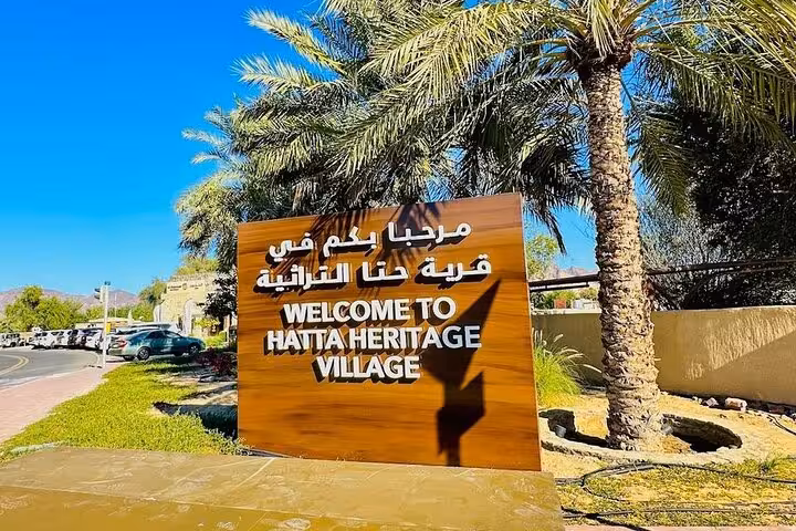 Welcome to Hatta Heritage Village sign under palm trees, stop on private full-day Hatta tour 1–6 pax