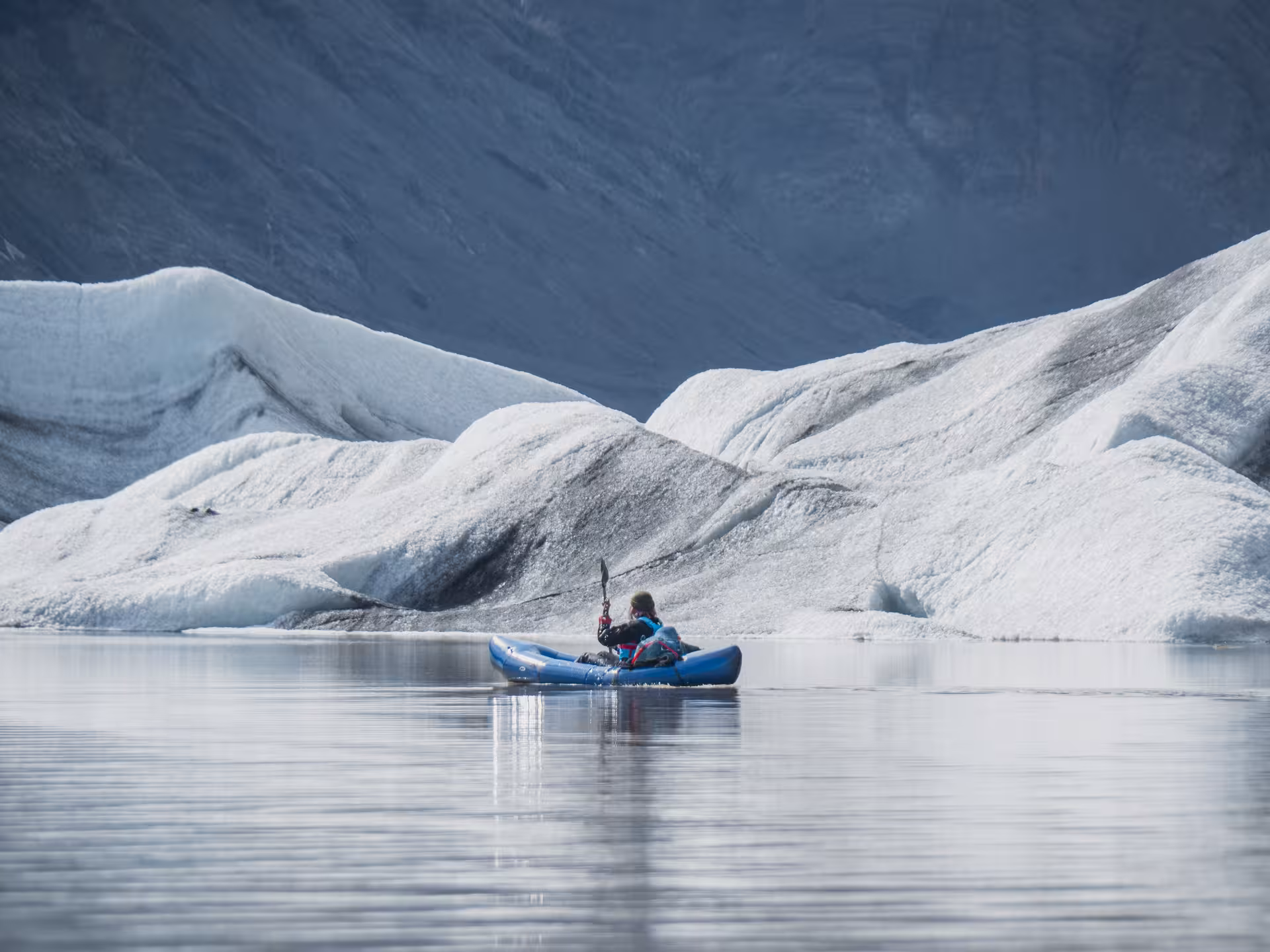 Solo kayaker gliding past sculpted icebergs on Heinabergslón glacier lagoon, Iceland, on a kayak and hike adventure