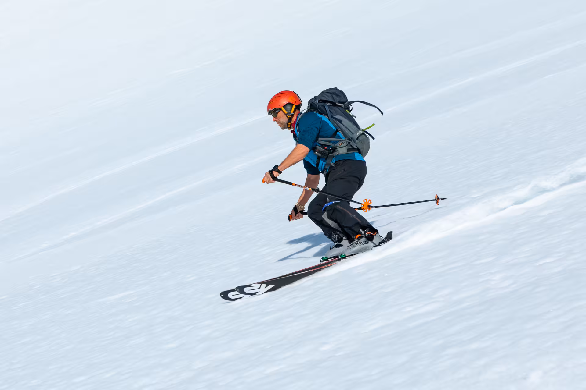 Skier in vibrant gear expertly descends snowy slope during a thrilling heli-skiing adventure.