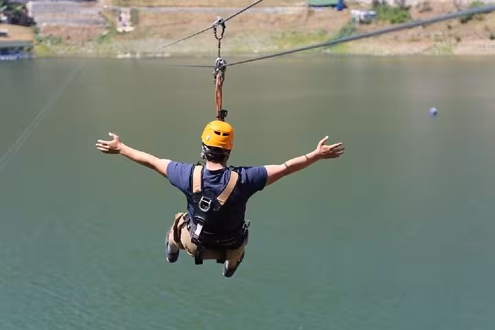 Helmeted rider ziplining over a lake on the Great Threesome rafting buggy zipline adventure tour
