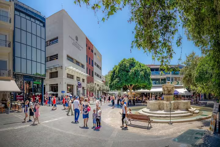Bustling square in Heraklion town with tourists exploring shops and a historic fountain, perfect for Knossos Palace tours.