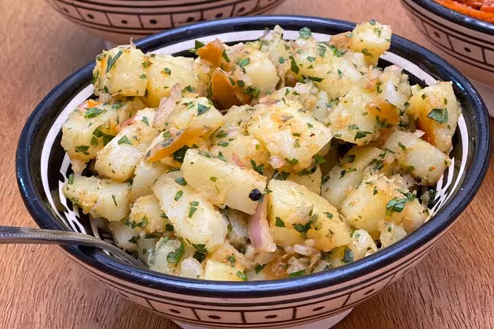 Herbed potato salad with fresh onions and parsley in a ceramic bowl, featured in a local cooking class experience.